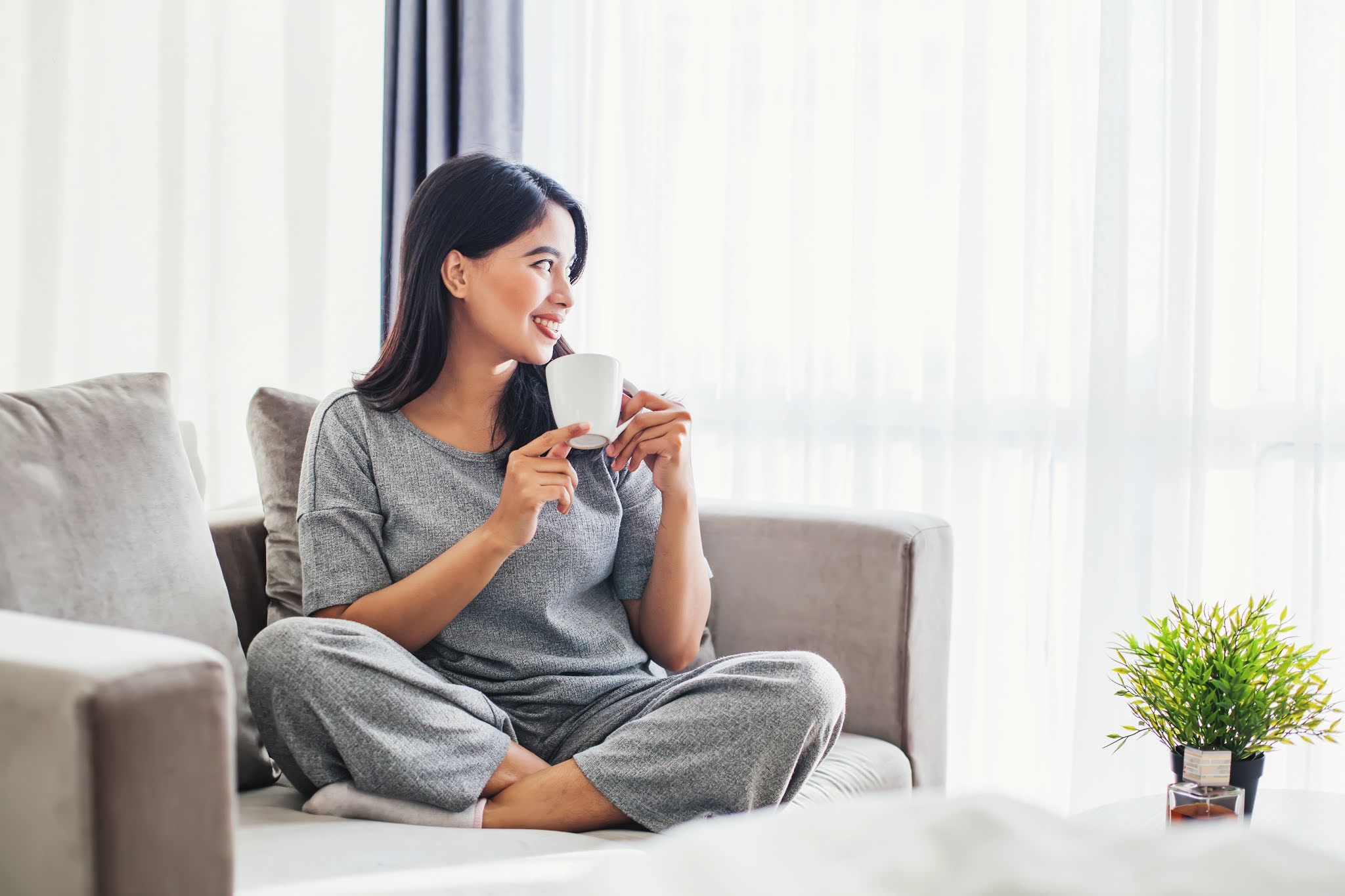 Young asian woman drinking coffee on a sofa bed at home